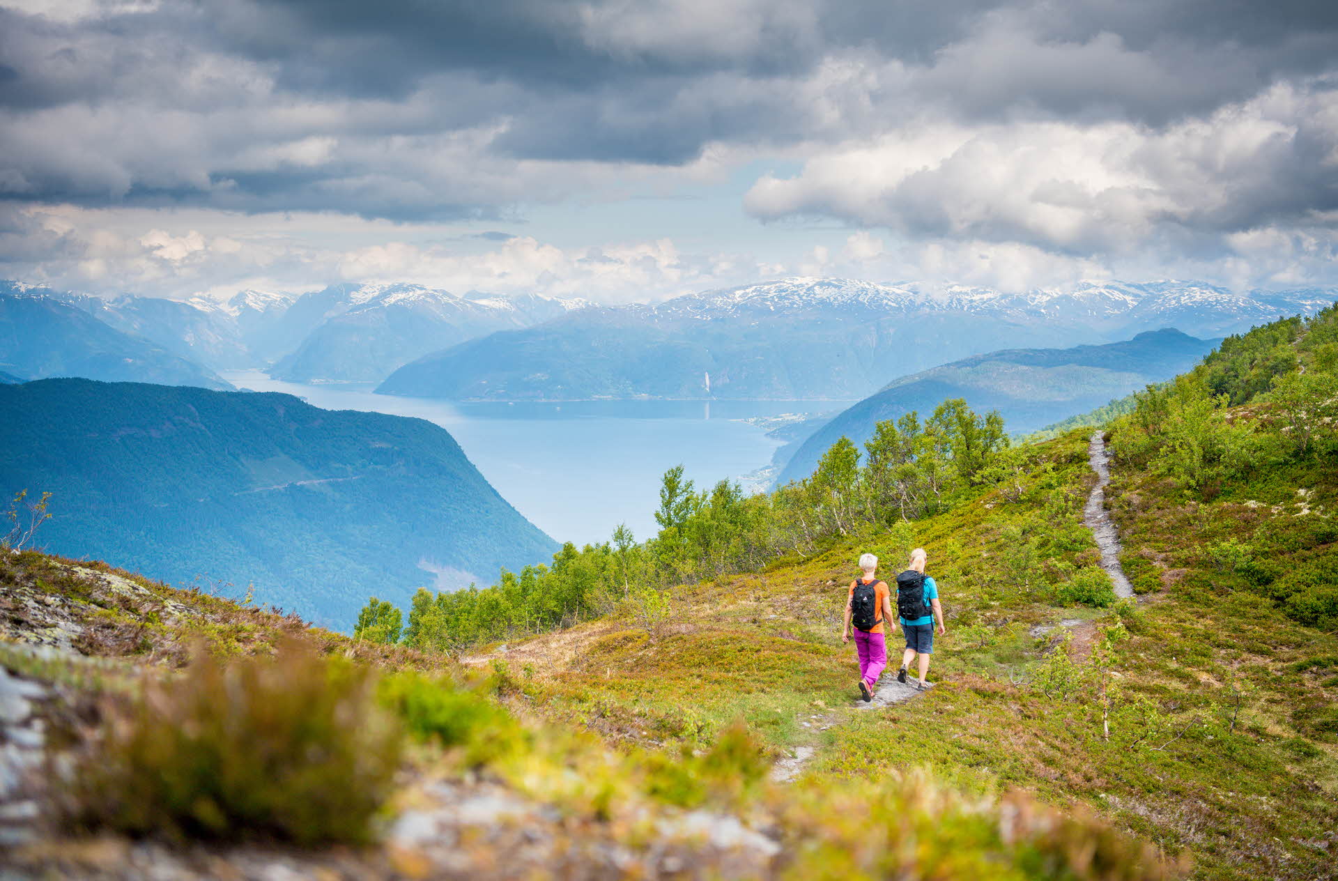 Two women walking on a mountain path, with Sognefjord in the background