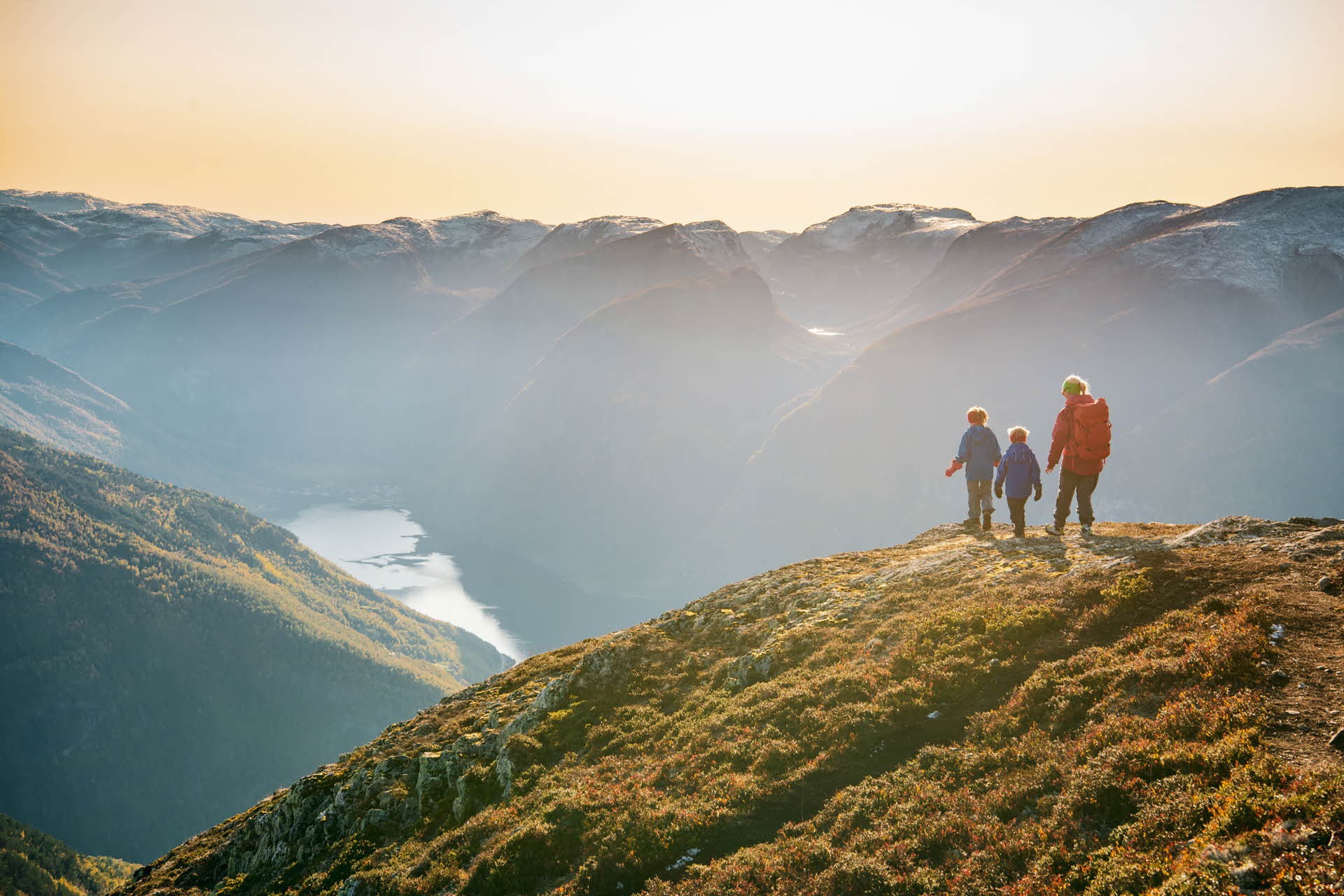 Une femme et deux enfants sur le mont Prest surplombant l’Aurlandsfjord, Flåm et les montagnes au coucher du soleil