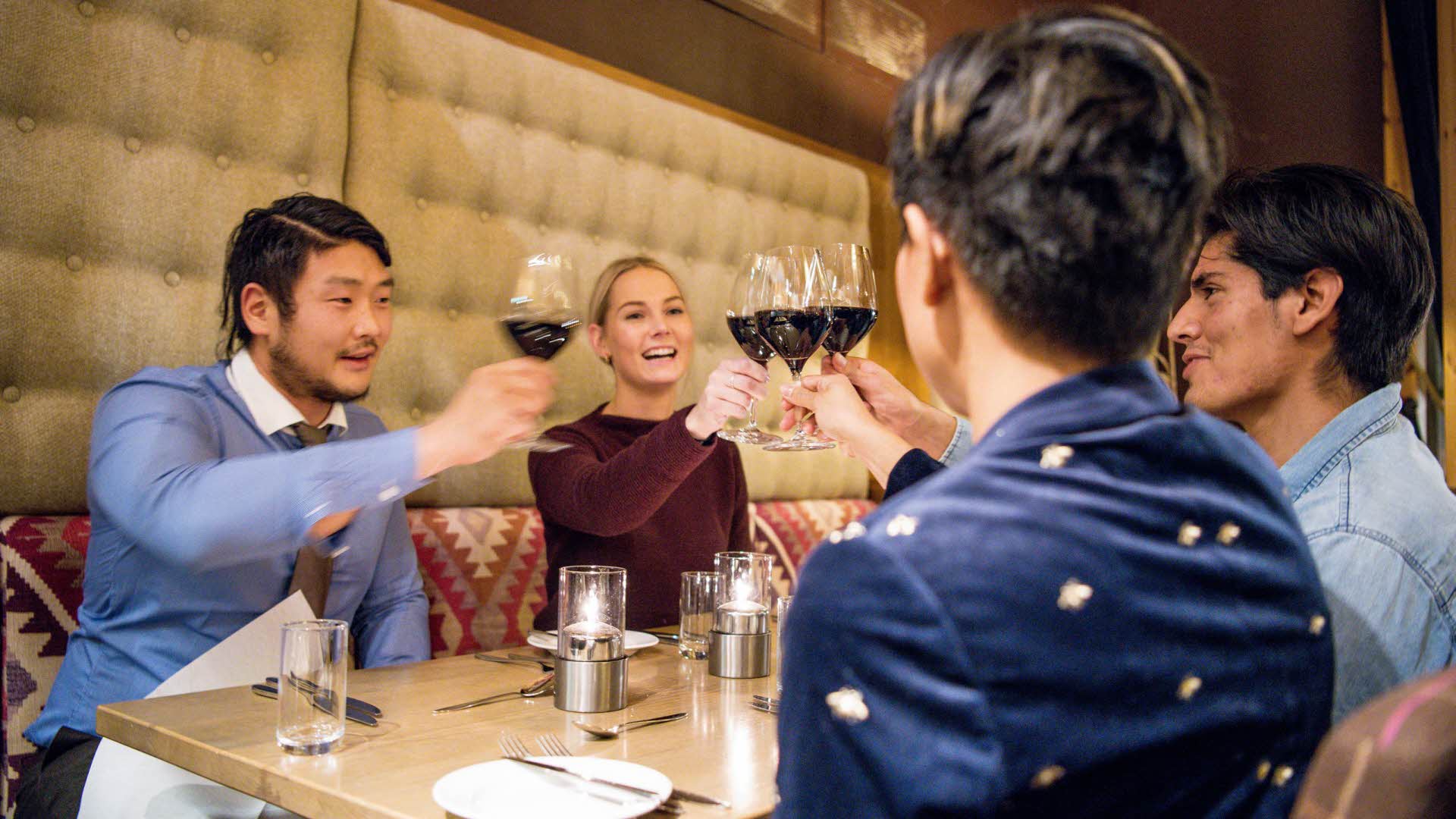 Zwei Paare stoßen mit Rotweingläsern an einem Tisch im Restaurant Arven an