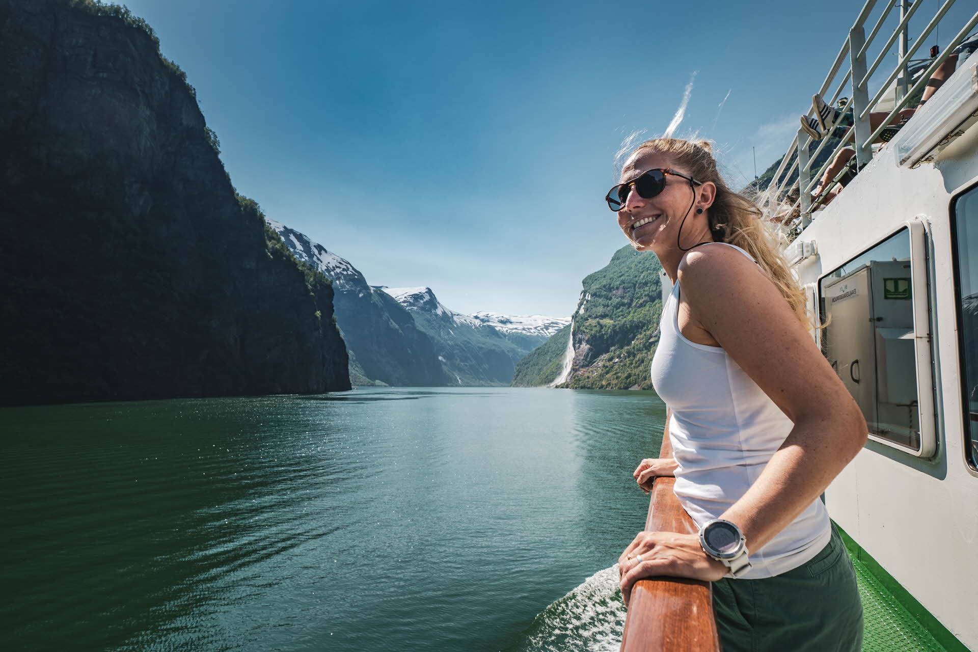 一名女子依靠在行驶在盖朗厄尔峡湾 (Geirangerfjord) 的渡轮的栏杆上，面带微笑