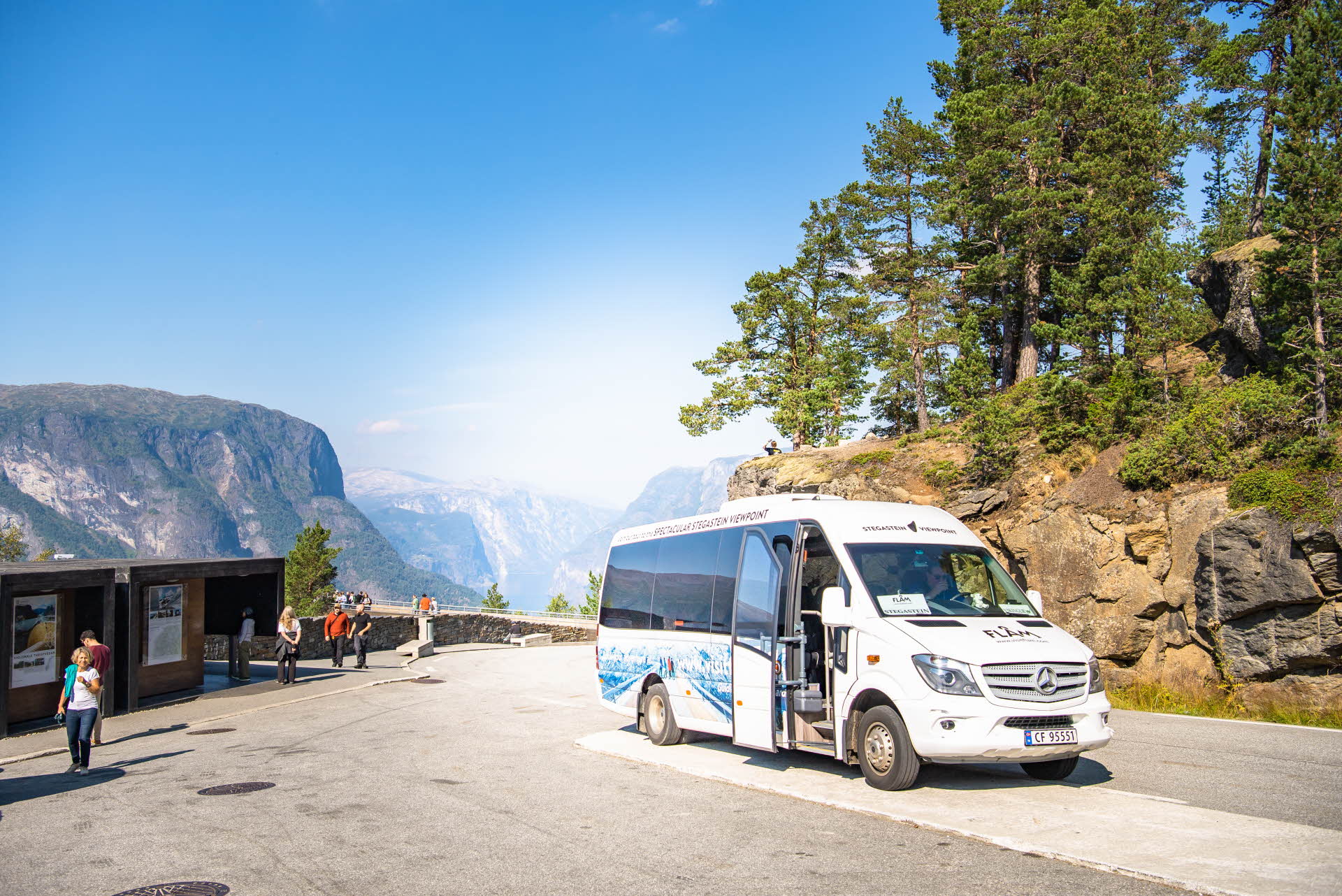 A shuttle bus next to a pine forest and views of mountains and a blue sky.
