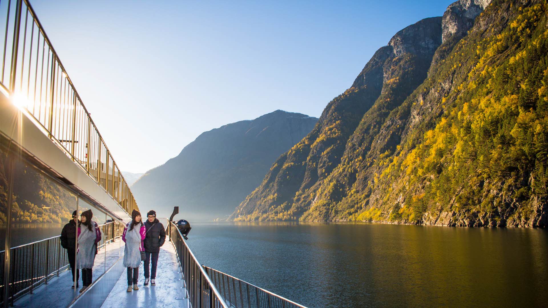 Two people walking down a walkway on a boat sailing by steep mountains on the Nærøyfjord.