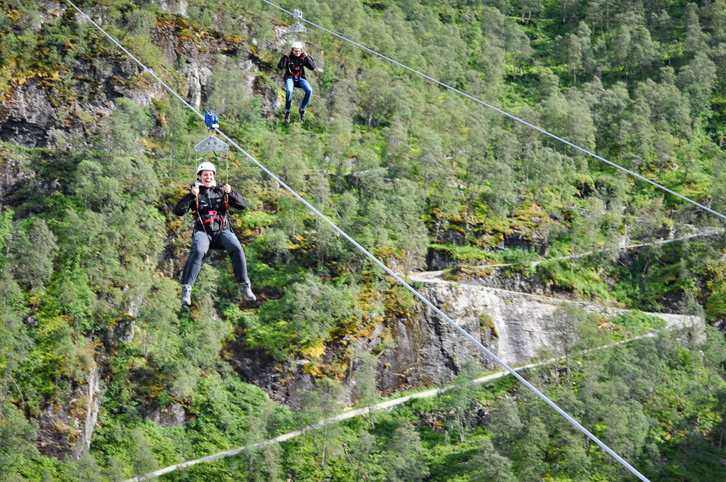 Deux personnes sur la tyrolienne de Flåm, avec les virages en épingle de la Rallarvegen à l’arrière-plan.