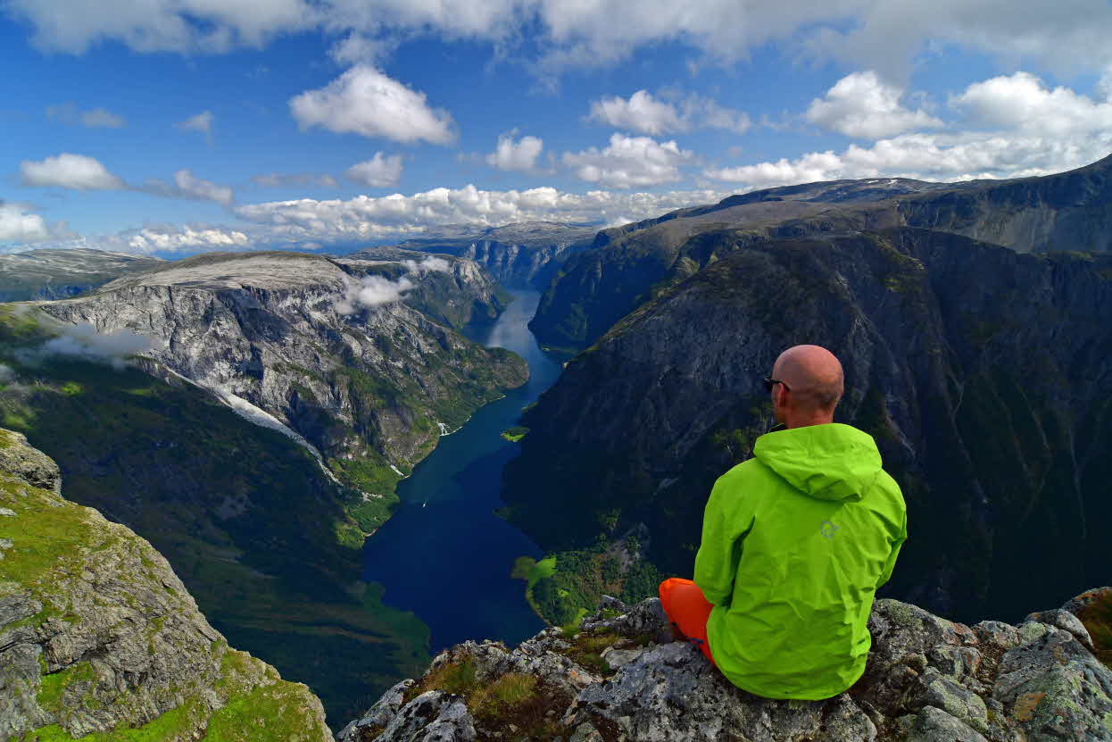 Ein Mann sitzt auf Bakkanosi und blickt auf den Nærøyfjord hinab
