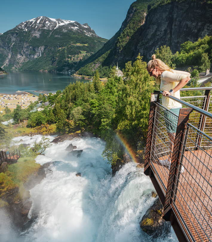A woman standing on a viewing platform over a waterfall in Geiranger