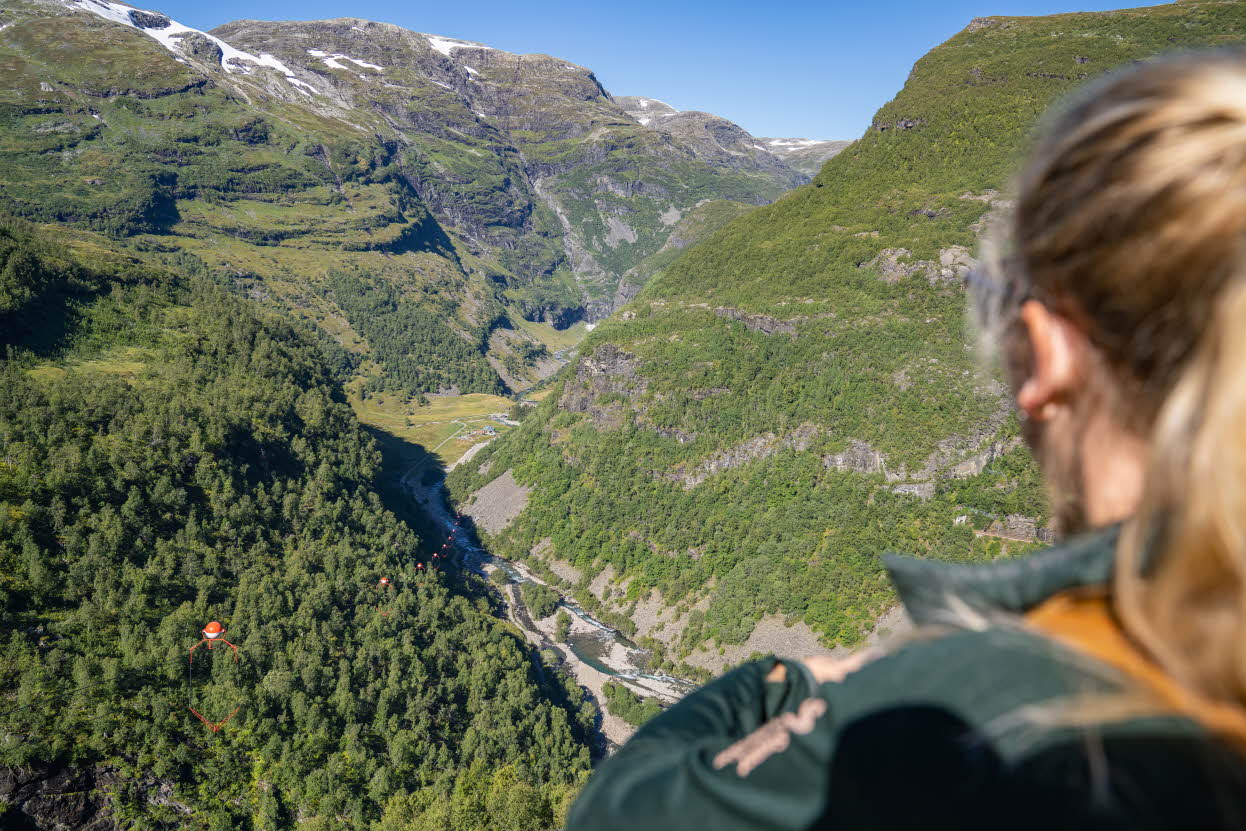 En kvinne med blond hestehale ser nedover Flåm zipline og Flåmsdalen