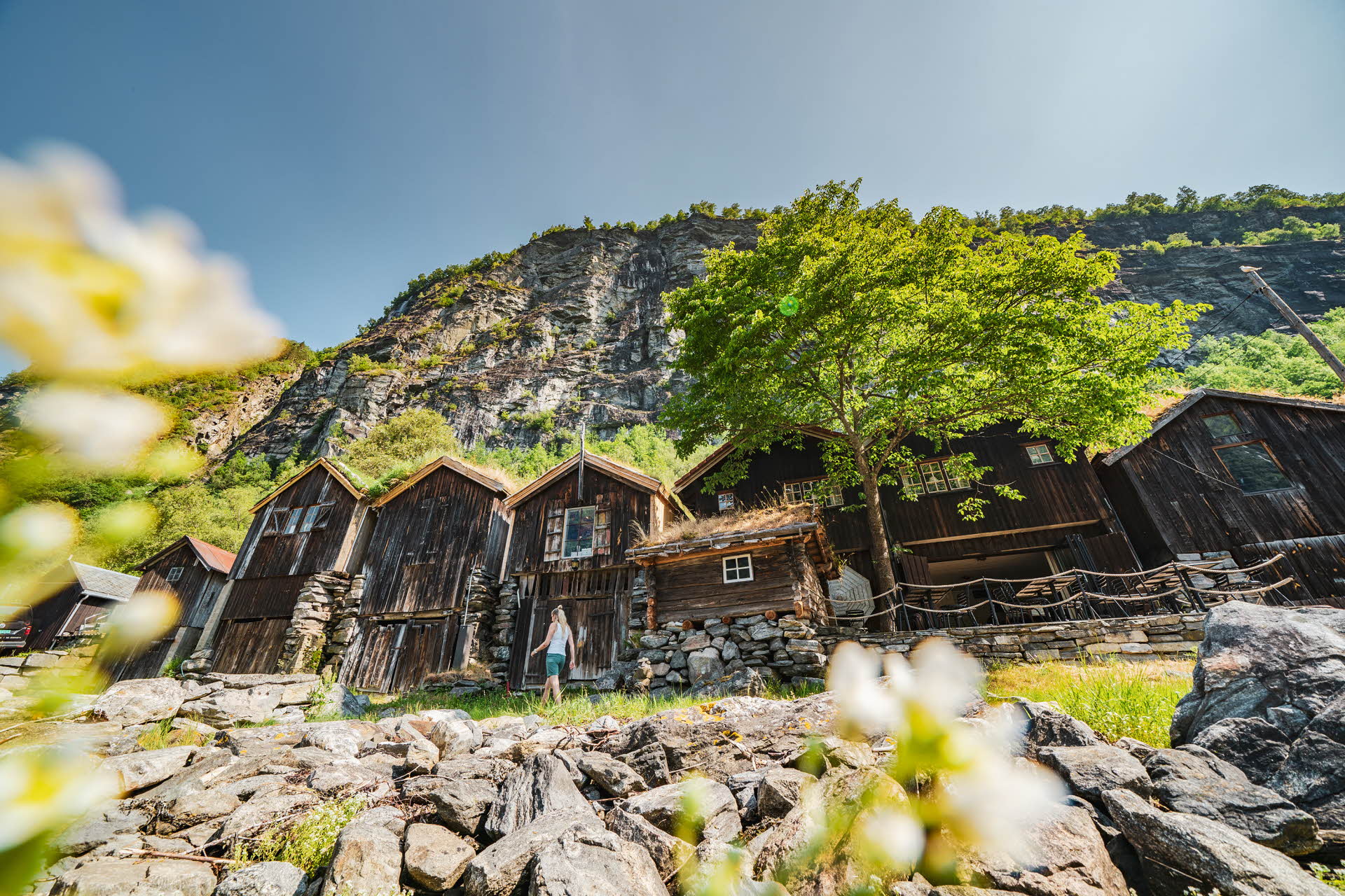 A woman walking next to old wooden houses in Geiranger