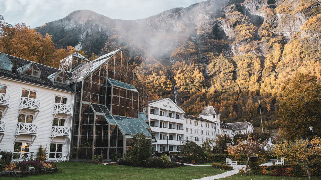 L’extérieur du Fretheim Hotel par une journée d’automne nuageuse, avec le jardin recouvert de brume en avant-plan et les montagnes en arrière-plan.