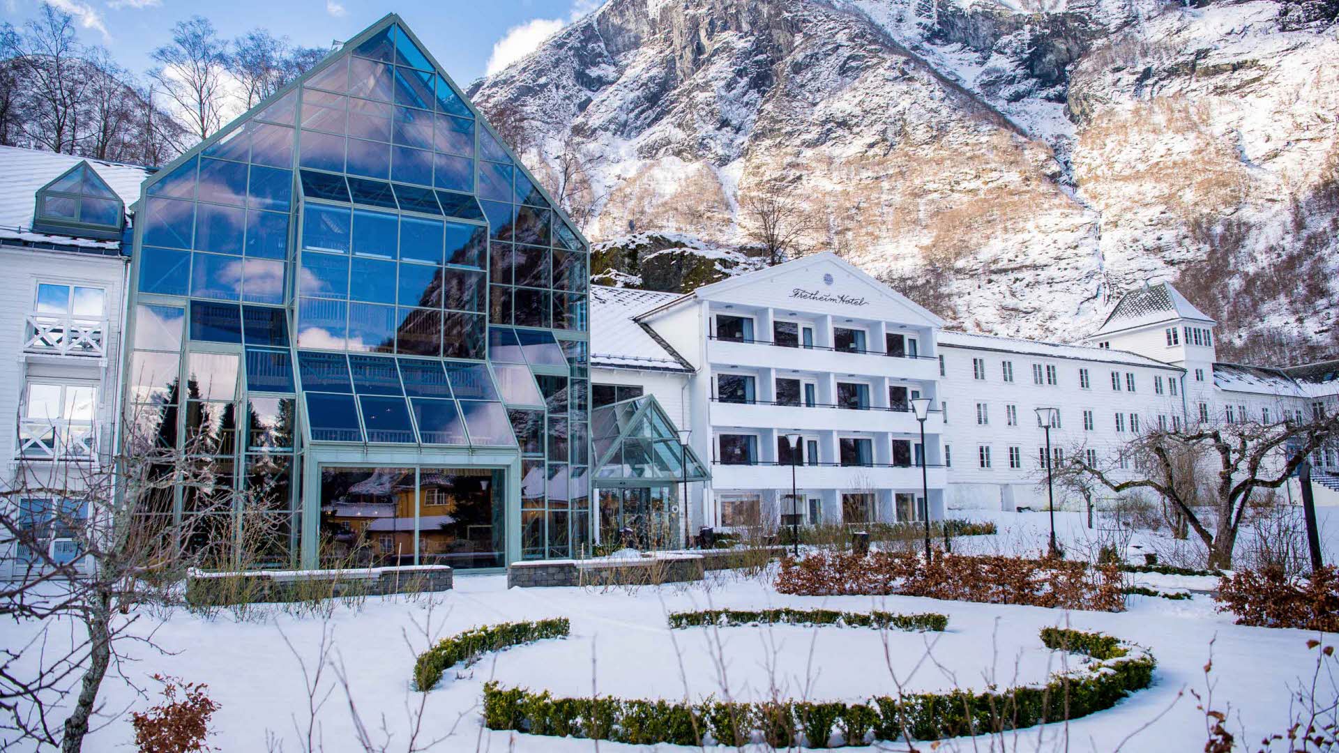 Das Hotel Fretheim mit einem verschneitem Garten im Vordergrund und weißen Bergen im Hintergrund.