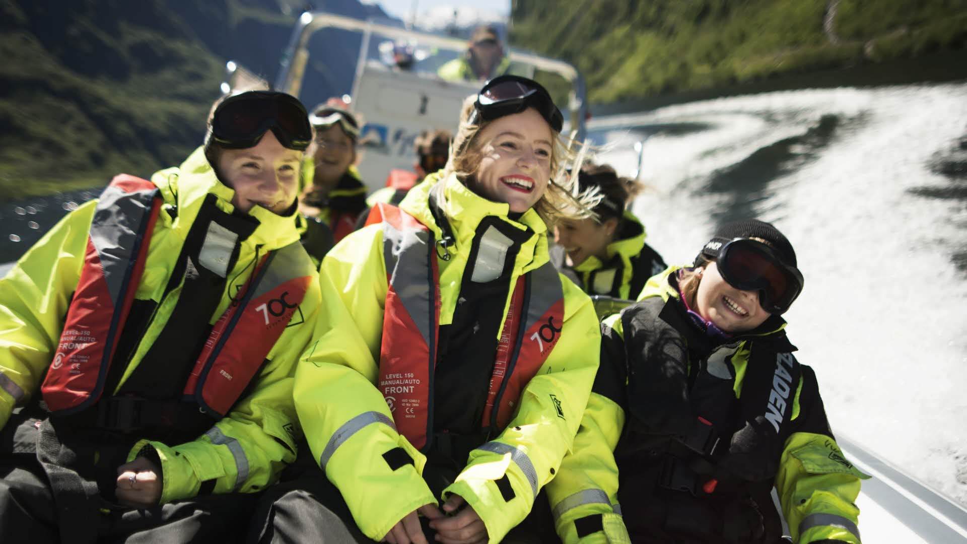 ネーロイフィヨルド(Naroyfjord)を全速力で航行するリブボートにウエットスーツに身を包んで座っている笑顔の3人