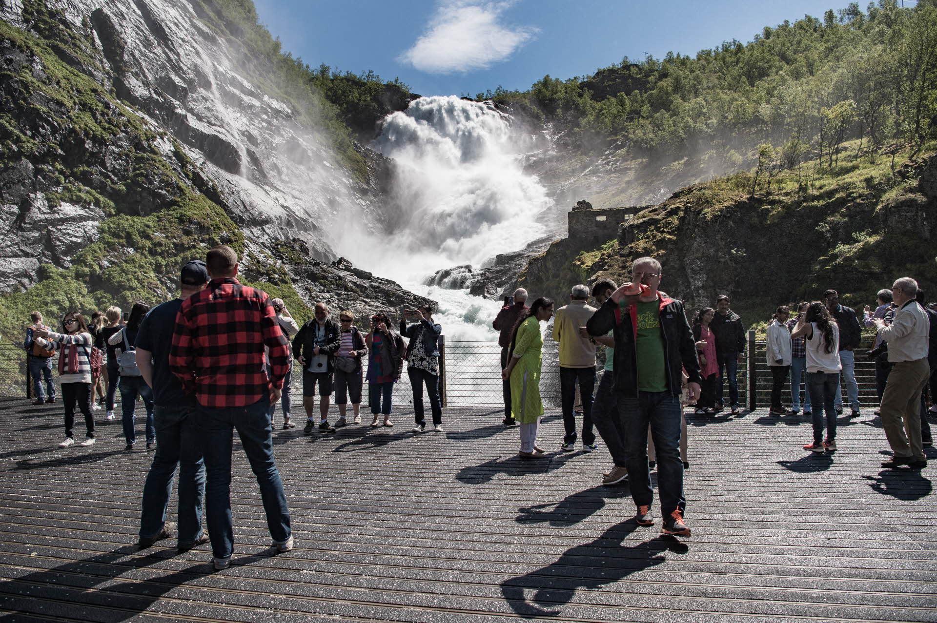 Eine Gruppe von Touristen steht im Sommer auf der Aussichtsplattform der Flåmbahn und blickt auf den tosenden Wasserfall Kjosfossen 