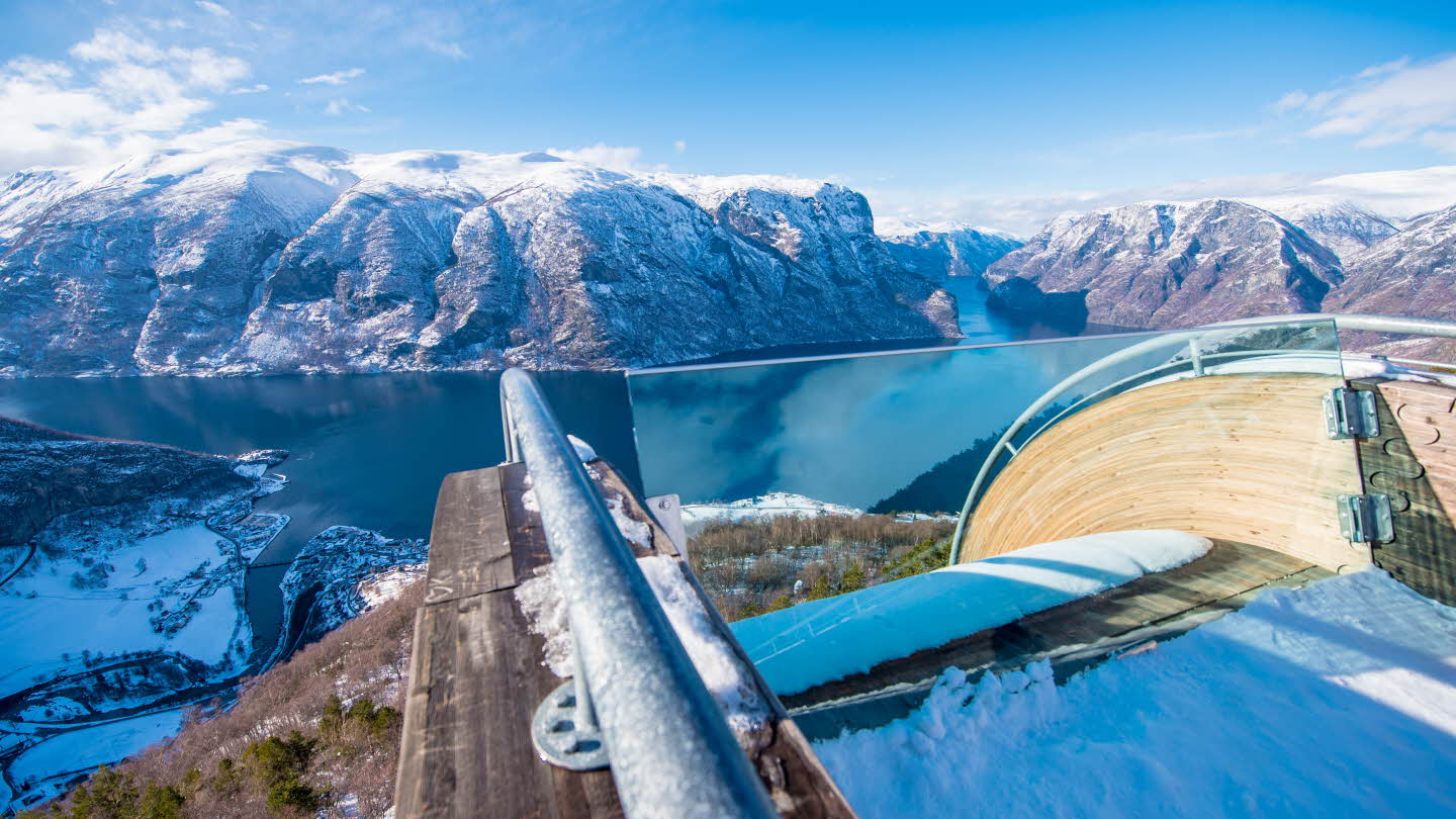 Front part of Stegastein Viewpoint with snow on it. View towards Aurlandsvangen, Aurlandsfjorden and snow-covered mountains. Blue sky.