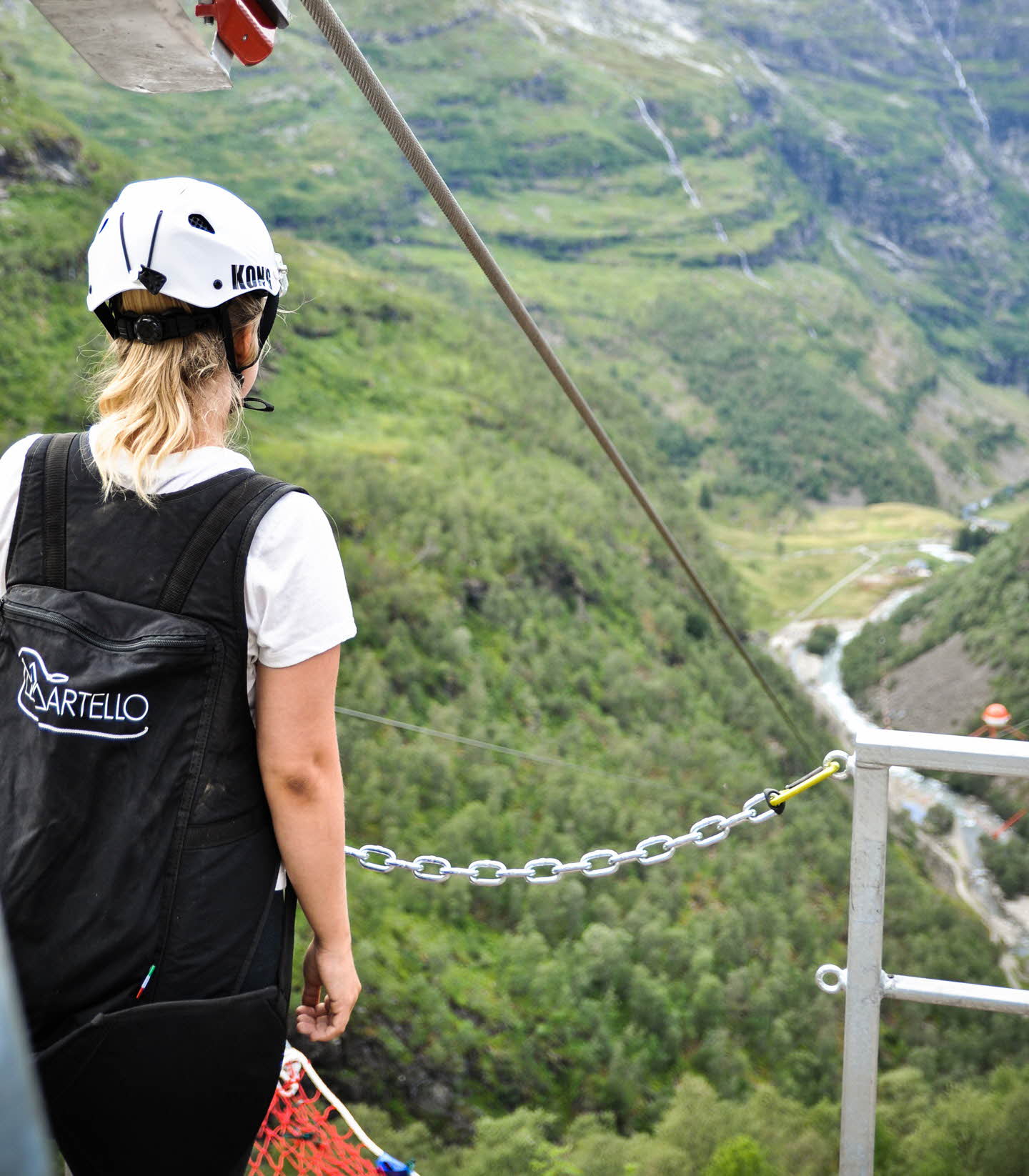 Una mujer con un arnés de seguridad y un casco mirando al valle de Flåm desde la plataforma de inicio de la tirolina de Flåm
