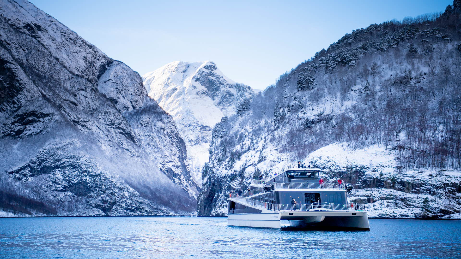 Un catamaran touristique devant des montagnes enneigées. 